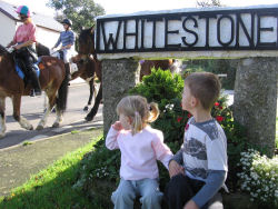 Whitestone sign with two small children and with horsespassing by